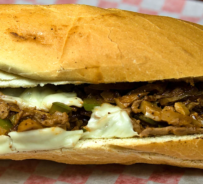 Philly cheese steak on a long roll with grilled meat, peppers, mushrooms and melted cheese