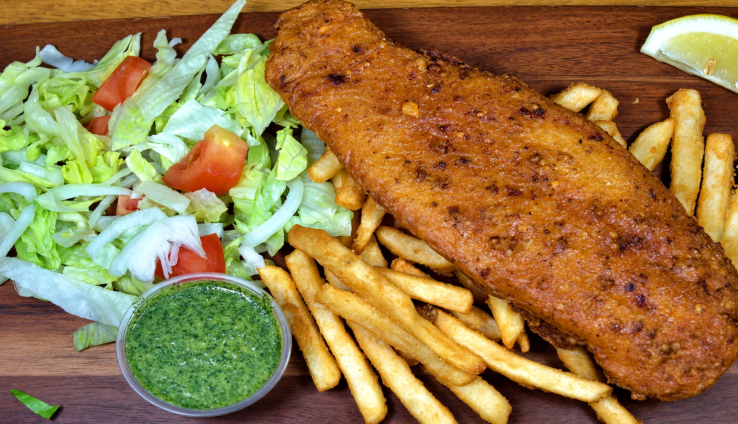 Spicy battered fish with fries, lettuce and tomato salad, green chutney and lemon