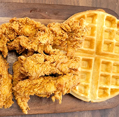 Chicken tenders beside a waffle on a wooden board
