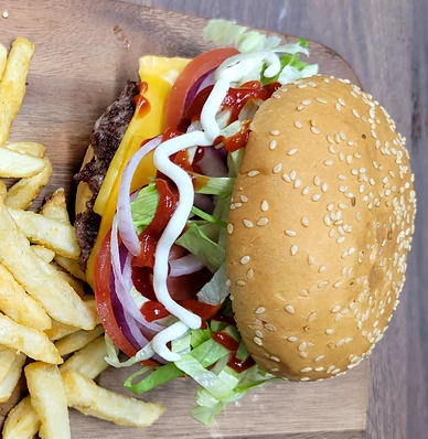 Cheeseburger with lettuce, tomato, onion and sauce beside fries, from above