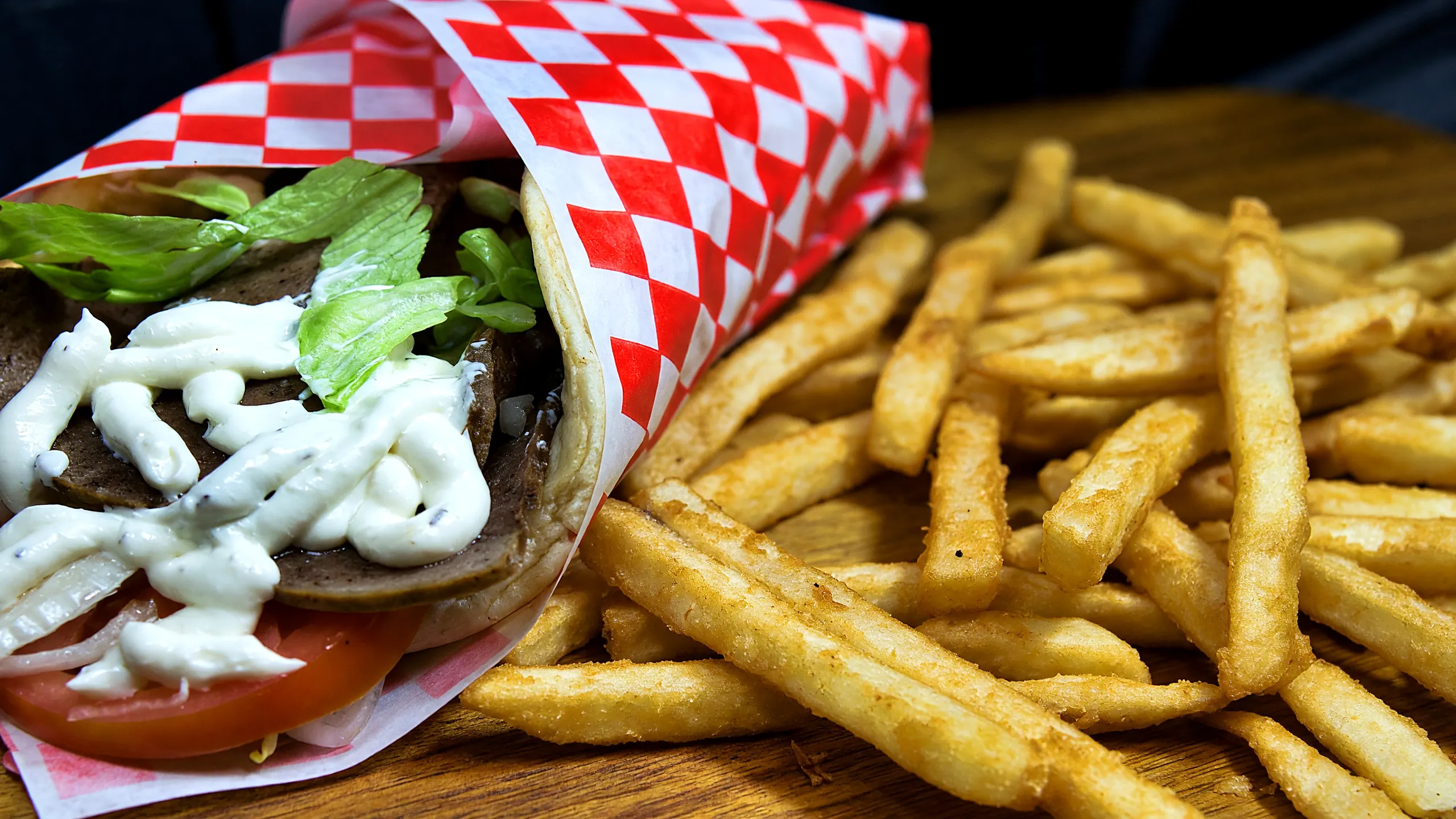 Gyro wrap with sliced meat, lettuce, tomato and garlic sauce, beside fries